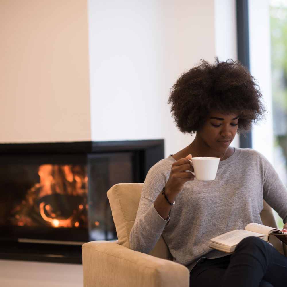 Woman Drinking Coffee and Reading a Book by the Fireplace